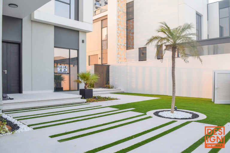 Palm tree-centered modern garden with clean white stones, geometric concrete and grass path, and minimalist architecture.