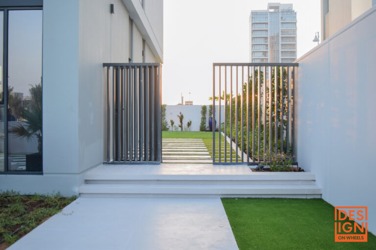 Contemporary landscape design with vertical slat gate, manicured lawn, pathway, and structured greenery leading to a garden area in Dubai.