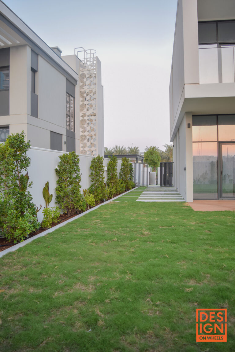 Modern garden with manicured lawn, sculpted hedges, and sleek architectural building with large glass windows by Design on Wheels.