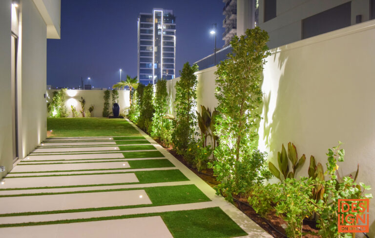 Contemporary garden with illuminated pathway, structured tropical greenery, and ambient lighting in a modern Dubai residence.
