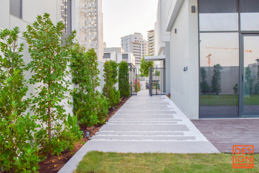 Sleek urban landscape design with concrete-and-gravel path, lush tropical planting, and gated entrance by Design by Design on Wheels.