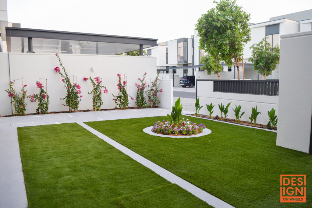 Modern landscaped garden with green lawn, flower beds, and climbing plants against a white wall.