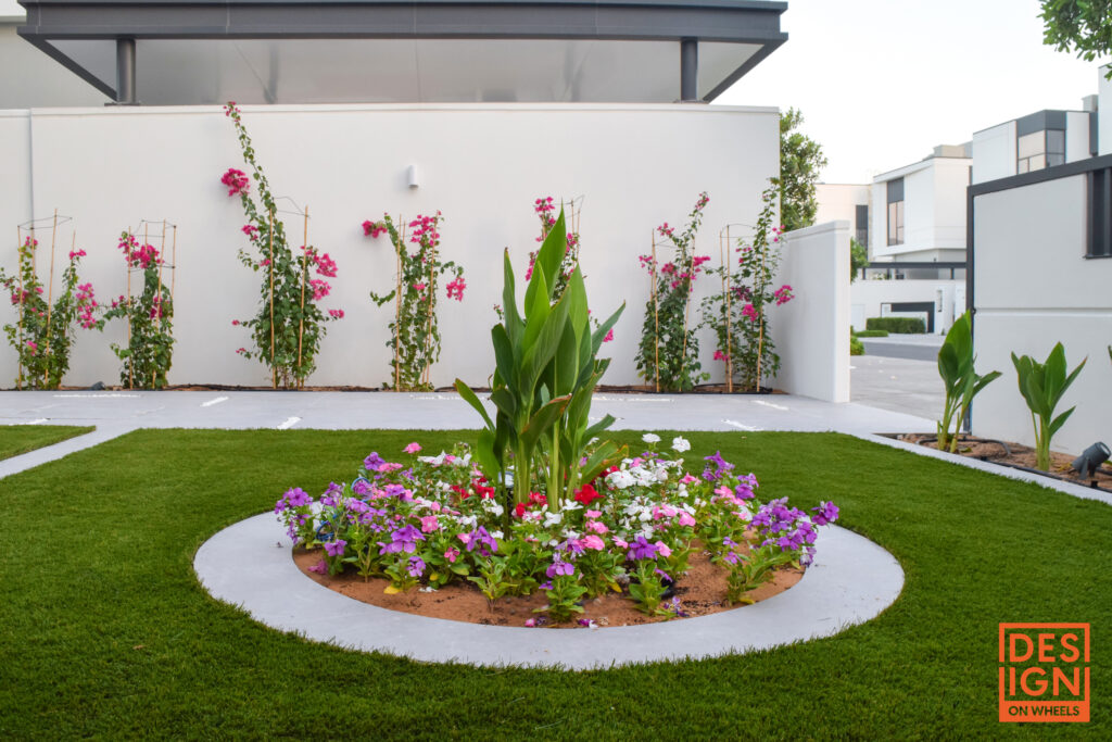 Circular flower bed with colorful blooms and tropical greenery surrounded by manicured lawn and modern architecture in Dubai.