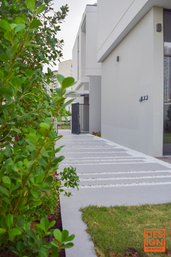 Minimalist outdoor pathway with concrete slabs and white gravel, bordered by tropical shrubs and green lawn leading to a modern building.