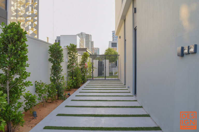 Contemporary outdoor walkway with concrete-and-grass strips, lush greenery, and black gate by Design Solutions.