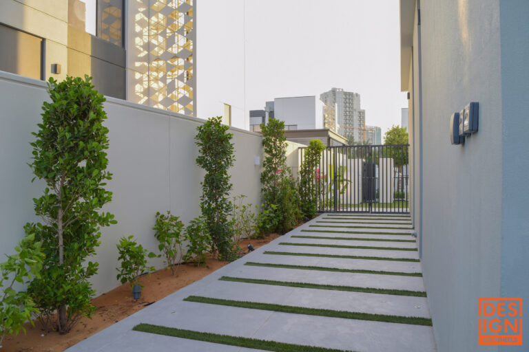 Urban garden walkway with concrete-and-grass path, tropical plants, and secure metal gate by Design Networks.