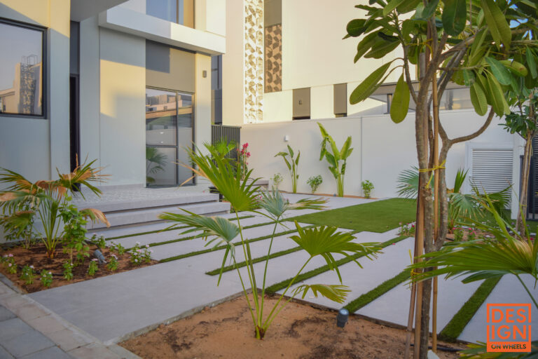 Modern house exterior with lush tropical landscaping, concrete path, and palm trees by Design on Wheels.