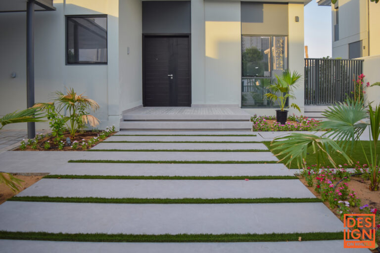 Contemporary house entrance with black door, tropical landscaping, and a modern concrete-and-grass pathway.