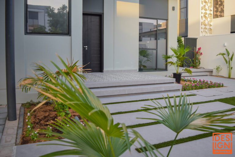 Stylish modern house entrance with tiled stairs, black door, and lush tropical landscaping.