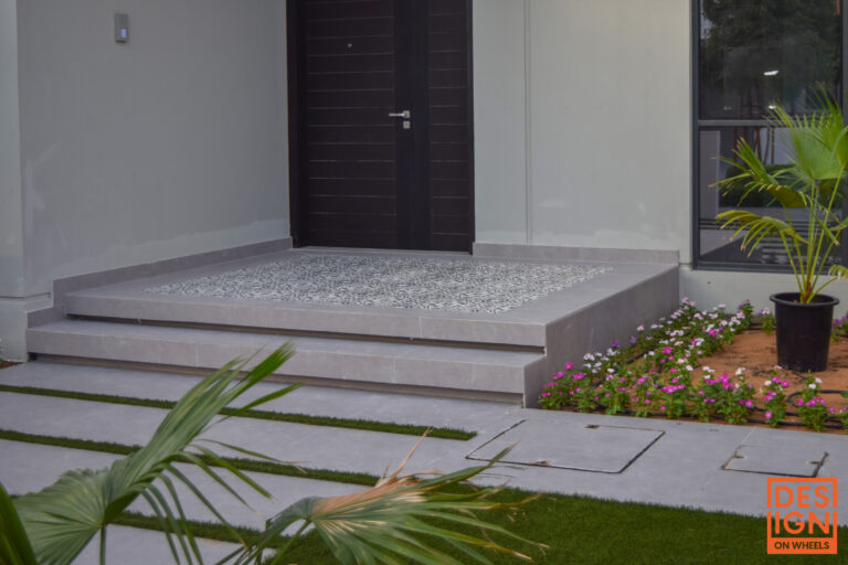 Elegant modern home entrance with a dark wood door, stone steps, and landscaped flower garden.