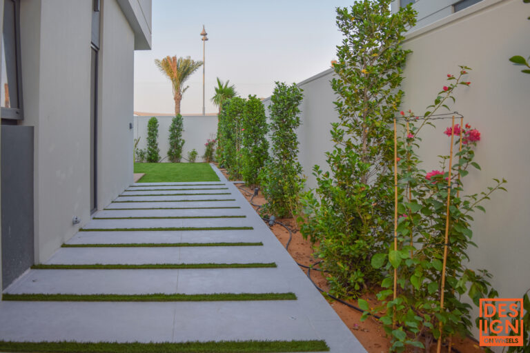 Contemporary garden walkway in Dubai with alternating concrete slabs and grass, surrounded by lush greenery.