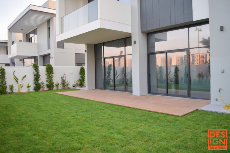 Luxury modern house in Dubai with floor-to-ceiling glass doors, wooden deck, and landscaped backyard.