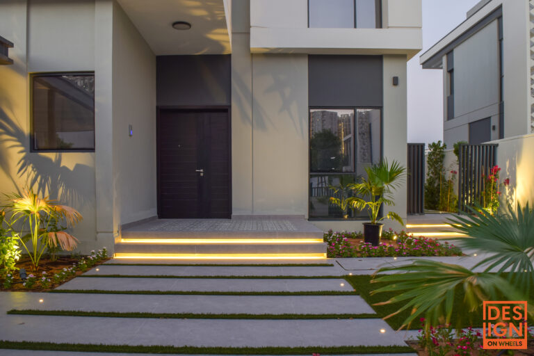 Modern villa entrance with artificial grass, soft step lighting, and focused spotlights on plants for a dramatic nighttime look.