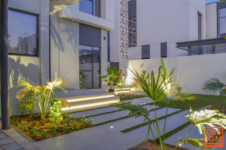 Modern villa entrance with artificial grass, soft step lighting, and focused spotlights on plants for a dramatic nighttime look.