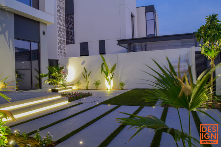 Modern villa entrance with artificial grass, soft step lighting, and focused spotlights on plants for a dramatic nighttime look.